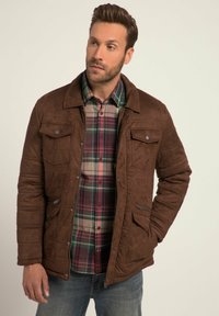 Brown suede jacket with a quilted design, featuring two chest pockets and a zip pocket. Underneath, a plaid shirt in green and burgundy.