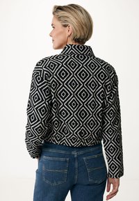 Svart och vit mönstrad jacka med diamantdesign, hög krage och åtsittande form. Matchas med jeans.
