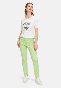 Chemise blanche à manches courtes avec un graphique de cœur léopard bleu et vert, associée à un pantalon skinny vert clair et des baskets blanches.