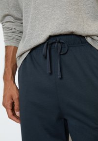 Pantalon de survêtement bleu marine avec cordon de serrage, texture lisse, taille élastique et coupe décontractée, associé à un t-shirt à manches longues gris.