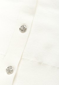 White knitted cardigan featuring a smooth texture, ribbed accents, and a silver button with an embossed design at the closure.