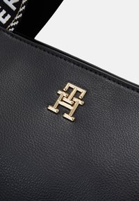 Sort læderhåndtaske med en metallisk guld logo accenter. Teksturen er pebret, med kontrasterende syning og en mønstret rem.