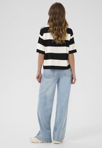 Zwart-wit gestreepte top met korte mouwen gecombineerd met lichtblauwe wijde jeans. De stof lijkt zacht en heeft een losse pasvorm met een casual stijl.