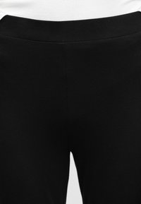 Pantaloni con fascia elasticizzata nera indossati con un top bianco, che mostrano l'area della vita e della parte superiore della coscia.