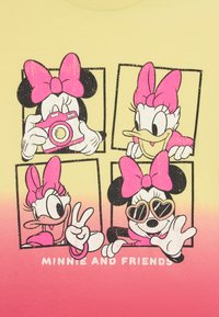 Camiseta amarilla con personajes de dibujos animados: Minnie y Daisy. La impresión muestra cuatro cuadros, con acentos en rosa brillante y poses juguetonas.