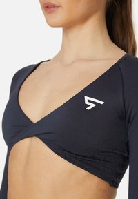 Navyblaues Langarmoberteil mit V-Ausschnitt, strukturiertem Material und weißem Logo auf der linken Seite. Mit einem Twist-Detail auf der Vorderseite.