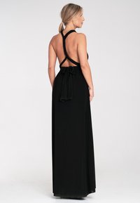 Czarna maxi sukienka z niskim dekoltem, halter neck i wiązaniem w talii. Materiał wydaje się gładki, z lekko opływającym krojem.
