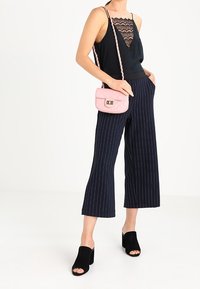 Černý tílko s krajkovým lemem, námořnické pruhované široké kalhoty, růžová prošívaná kabelka a černé sandály na blokovém podpatku.