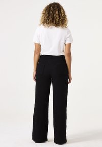 Pantalones negros de pierna ancha fabricados en tejido texturizado, con cintura alta y dos bolsillos traseros, combinados con una camiseta blanca lisa.