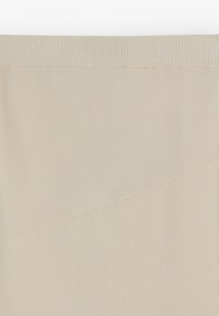 Tela beige con una textura suave que presenta un patrón acanalado en la parte superior. El diseño tiene una costura asimétrica a lo largo de un lado.