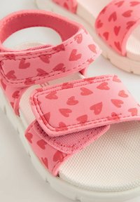 Rosa sandaler med hjärtmönster; justerbara kardborreband; texturerad vit innersula; mjukt material; gummisula.