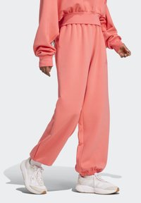 Ružové tepláky s voľným strihom, elastickým pásom a manžetami. Majú bočné vrecká, sú vyrobené z mäkkej látky s hladkou textúrou.