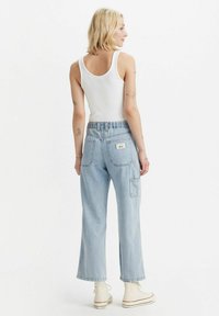 Pantaloni in denim azzurro chiaro a gamba larga con vita alta, tasche posteriori e vestibilità rilassata. Indossati con una canotta bianca e sneakers bianche.