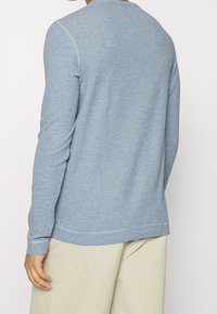 Ljusblå långärmad skjorta i mjukt tyg, med rundad halsringning, ribbade ärmslut och en avslappnad passform, visad framifrån.