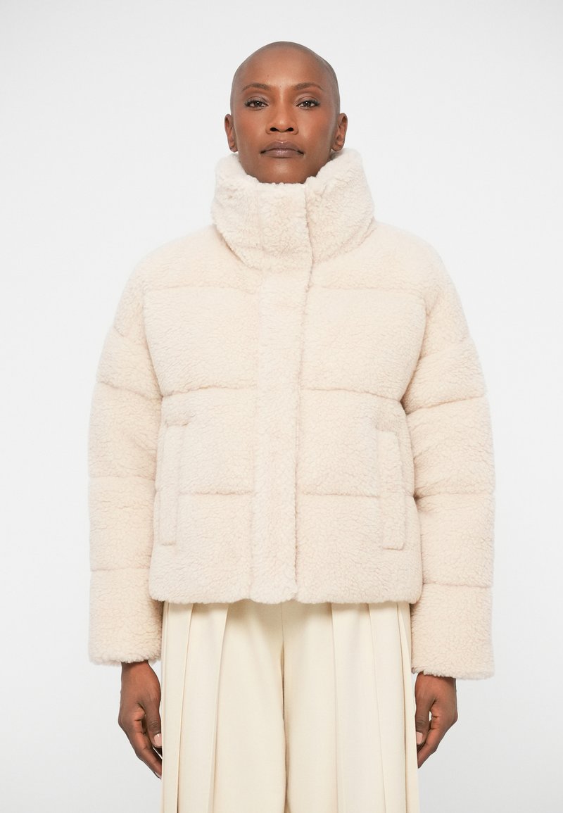 Cream-colored, fluffy, quilted jacket with a high collar, front pockets, and a boxy silhouette. Features soft texture and minimal design.