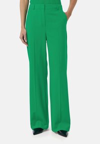 Pantalons larges verts en tissu lisse, dotés d'une taille haute, de plis et de poches latérales. Associés à des talons noirs pointus.