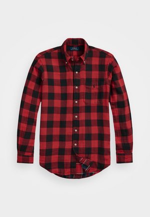 Camisa de manga larga con botones, de cuadros rojos y negros, con bolsillo en el pecho y cuello abotonado, extendida sobre un fondo blanco.