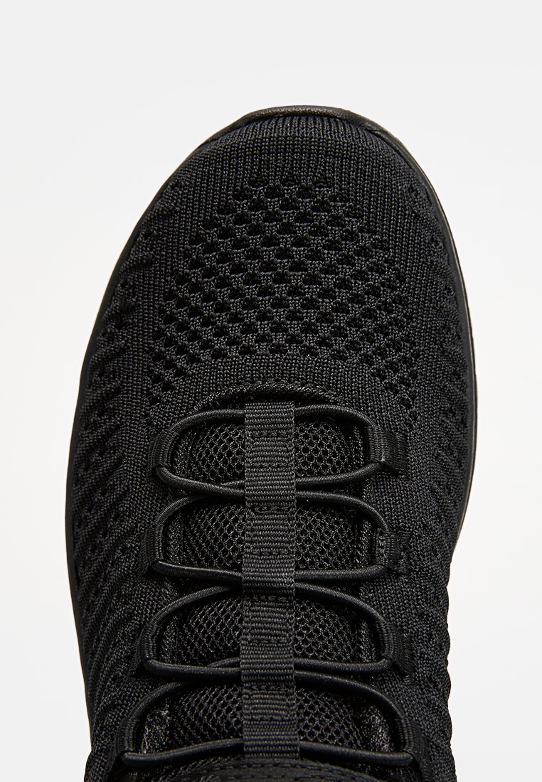 Nahaufnahme der Spitze eines Sneakers aus schwarzem Strickstoff mit integrierten Schnürschlaufen und atmungsaktiven Mesh-Details.