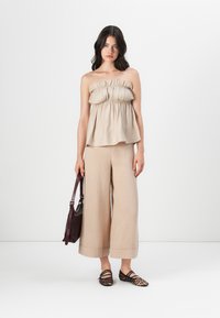 Lys beige strapless topp med innsamlet detalj, løst snitt. Brede beige bukser med mansjetter, parret med brune og svarte mønstrede leiligheter.