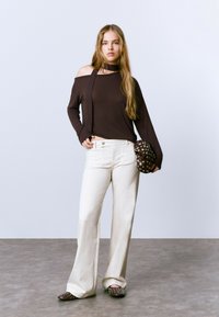 Blusa marrón de manga larga y cuello off-shoulder, pantalones blancos de pierna amplia, bolso marrón con tachuelas y zapatos marrones. Texturas suaves con un diseño casual.