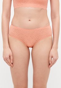 Set di lingerie color pesca con un design testurizzato, caratterizzato da bordi ondulati sul reggiseno e sui briefs a vita alta.