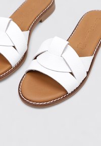 Sandalias deslizantes de cuero blanco con diseño de tira trenzada, plantilla acolchada marrón y detalles de costura a lo largo del borde de la suela.