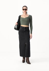 Grønn ribbestrikket genser med lange ermer og v-hals, svart denim maxiskjørt med frontsliss, brune hælboots og svart håndveske. Fasjonabel og moderne.