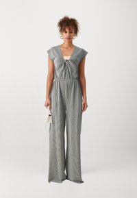 Combinaison rayée grise avec un décolleté en V profond, des manches courtes et un lien à la taille. Coupe ample avec un pantalon large.