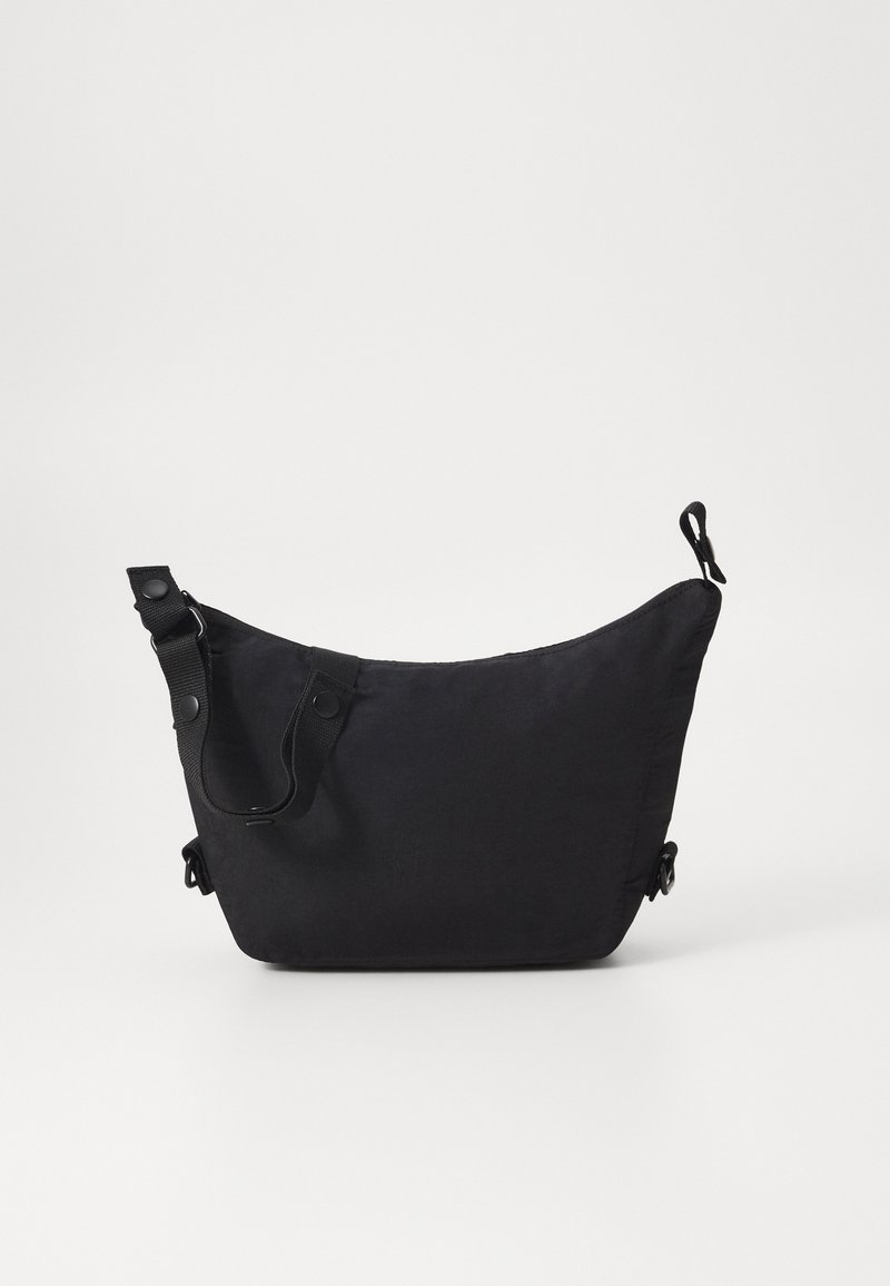 Black fabric shoulder bag with a curved shape, adjustable strap, snap button accents, and a smooth texture. No visible patterns.