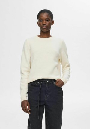 Cream-colored knitted sweater with a round neck and long sleeves, paired with high-waisted black denim jeans featuring a drawstring waist.