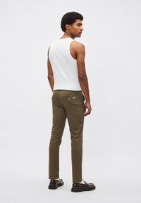 Witte mouwloze tanktop, olijfgroene slim-fit broek, gladde stof, met achterzakken en subtiele details; zwarte schoenen.
