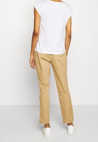 T-shirt en coton blanc à manches courtes style casquette, associé à un pantalon chino beige et des baskets blanches. La tenue est décontractée et ample.