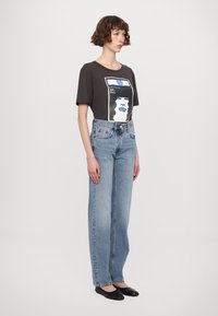 Grafika marškiniai tamsiai pilkos spalvos, pagaminti iš medvilnės, su spalvingu veido spauda; aukšto liemens šviesiai mėlynos džinsai; juodi butai; lygi tekstūra; laisvas kirpimas.