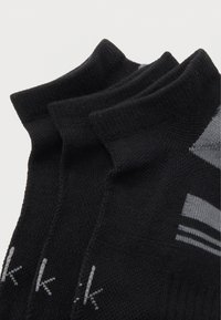 Τρία ζευγάρια μαύρες αστραγάλες κάλτσες με γκρι λεπτομέρειες και ένα μικρό λογότυπο "k" τοποθετημένα δίπλα το ένα στο άλλο σε λευκό φόντο.