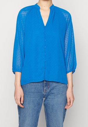 Blusa blu con bottoni, scollatura a V, motivo a pois testurizzato, tessuto trasparente e maniche a tre quarti arricciate ai polsi.