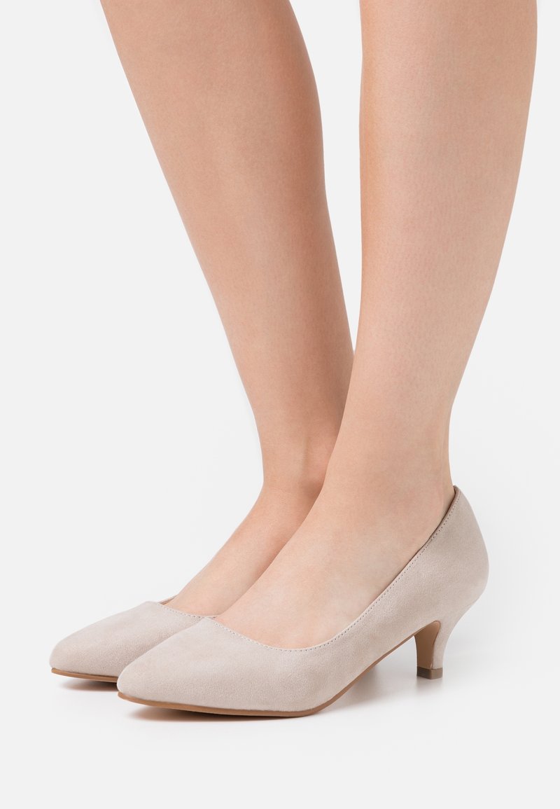 Chaussures à talons hauts en daim beige avec un bout pointu et un petit talon bloc, présentant une texture lisse et un design minimaliste.