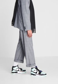 Šedý kostkovaný oblek s černým šátkem; na sobě má černé a mátově zelené vysoké tenisky s potiskem zvířat a černými tkaničkami.