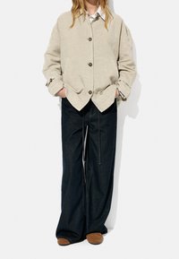 Beige linned knapjakke med to forlommer, parret med brede mørkeblå denim jeans og brune slip-on sko.