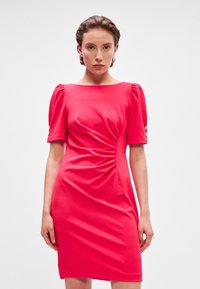 Priliehavá červená šaty typu sheath s krátkymi puff rukávmi, naberaním na živôtiku a gombíkovými akcentmi na manžetách rukávov. Hladká textúra tkaniny.