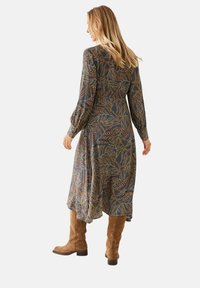 Vestido de manga larga con una tela azul oscuro que presenta un colorido patrón de hojas. Combinado con botas de ante marrón hasta la rodilla. Forma en A fluida.