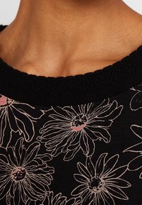 Schwarzer Stoff mit floralem Muster in hellrosa, ausgestattet mit einem gerippten schwarzen Ausschnitt. Das Design zeigt große Gänseblümchen mit detaillierten Konturen.