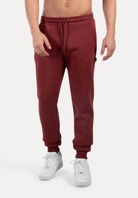 Pantalones de chándal burdeos con cintura el�ástica, cordón y puños acanalados, combinados con zapatillas blancas. Material suave, corte relajado.