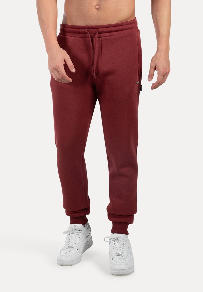 Pantalones de chándal burdeos con cintura elástica, cordón y puños acanalados, combinados con zapatillas blancas. Material suave, corte relajado.