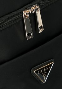 Zaino in nylon nero con doppia cerniera metallica dalla finitura lucida e patch triangolare con logo "GUESS" in testo argento.