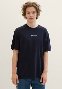 T-shirt in cotone blu navy con scollo rotondo e maniche corte. Presenta un logo bianco "DENIM TOM TAILOR" sul petto. Vestibilità casual.