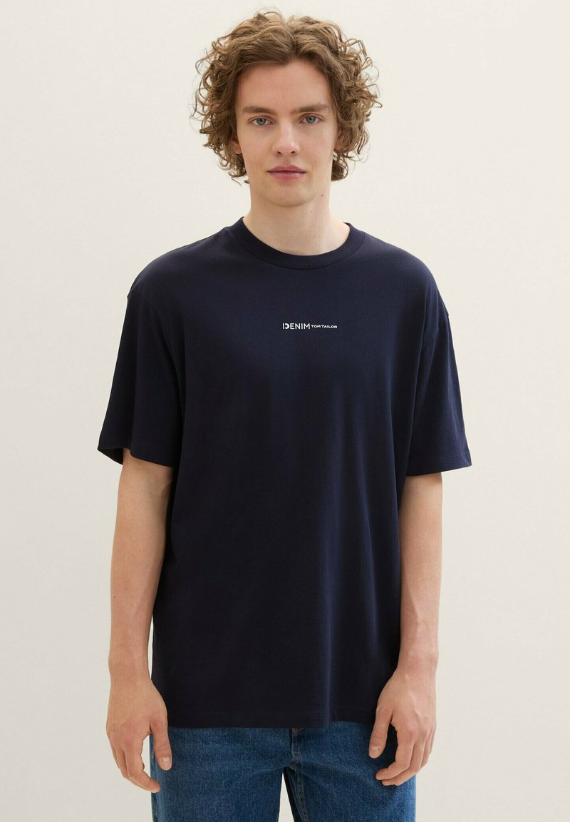 T-shirt in cotone blu navy con scollo rotondo e maniche corte. Presenta un logo bianco "DENIM TOM TAILOR" sul petto. Vestibilità casual.