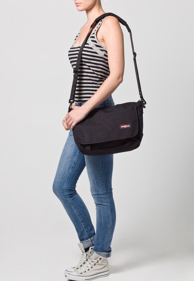 Borsa a tracolla nera realizzata in tessuto resistente, con un flap pieghevole, una tracolla regolabile e una patch con logo. Texture liscia con dettagli minimi.