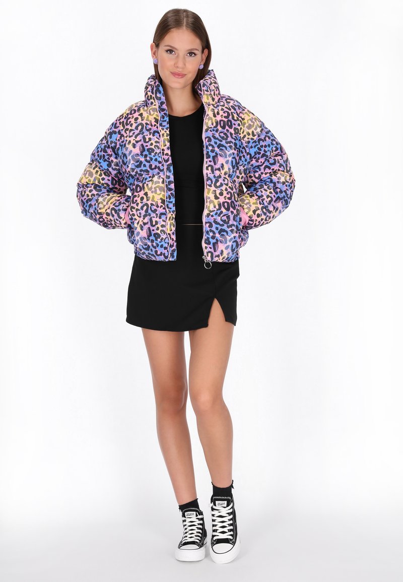 Barevná zkrácená péřová bunda s mnohobarevným leopardím potiskem, sezipovým uzávěrem a elastickými manžetami. Nositá přes černý top a sukni.