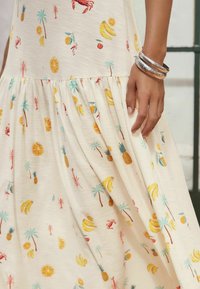 Robe évasée en tissu léger avec un motif coloré de fruits et de crabes sur fond crème, dotée d'une taille froncée et d'une texture côtelée.