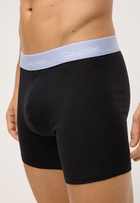 Čierne bavlnené boxerky s pásom v svetlomodrej farbe s logom Calvin Klein, ktoré majú priliehavý strih a hladkú textúru.